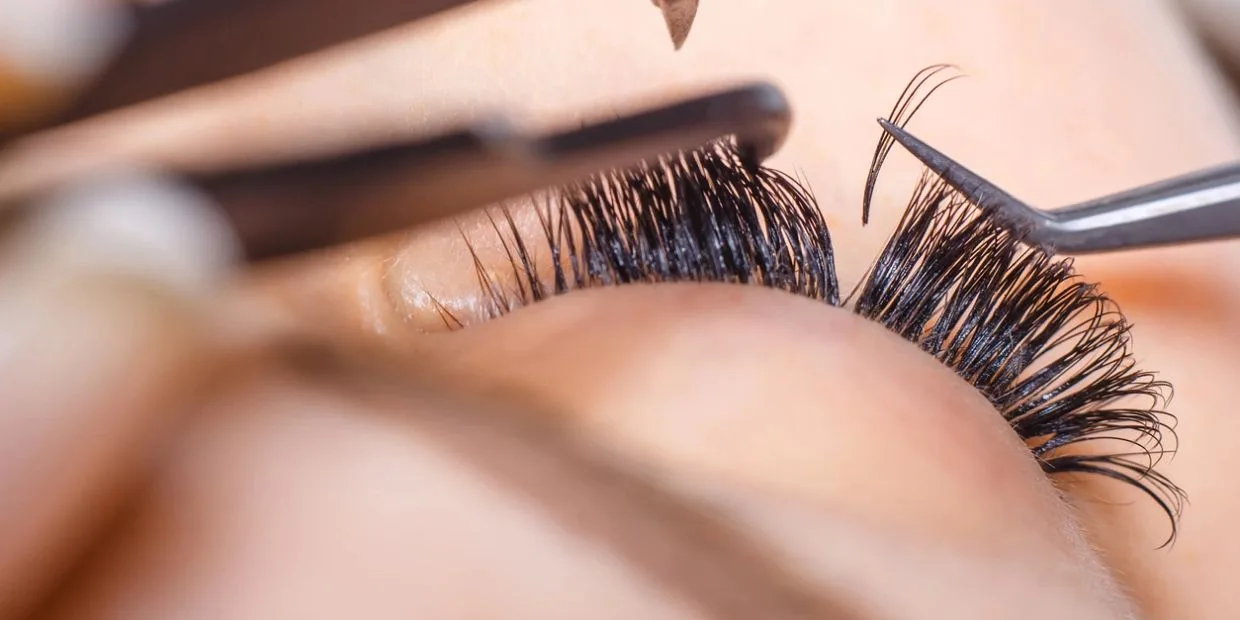 Lash extension application in progress — tweezers isolating a single natural lash